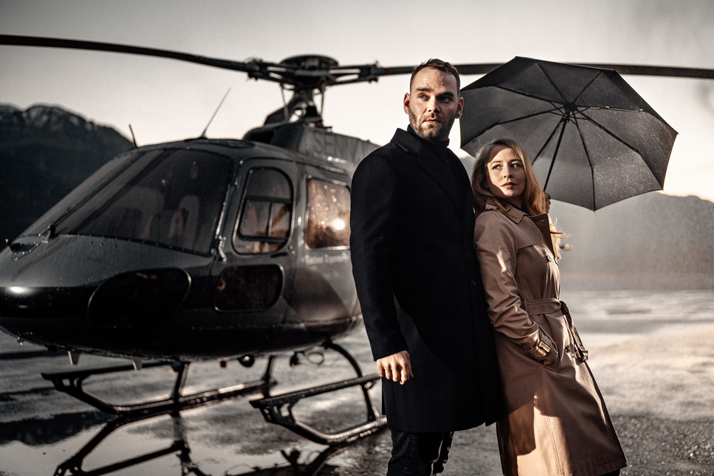 Mann und Frau unter schwarzem Regenshchirm vor Hubschrauber